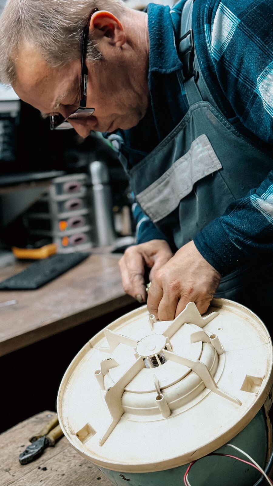 Technician in overalls working on a round appliance housing at the bench