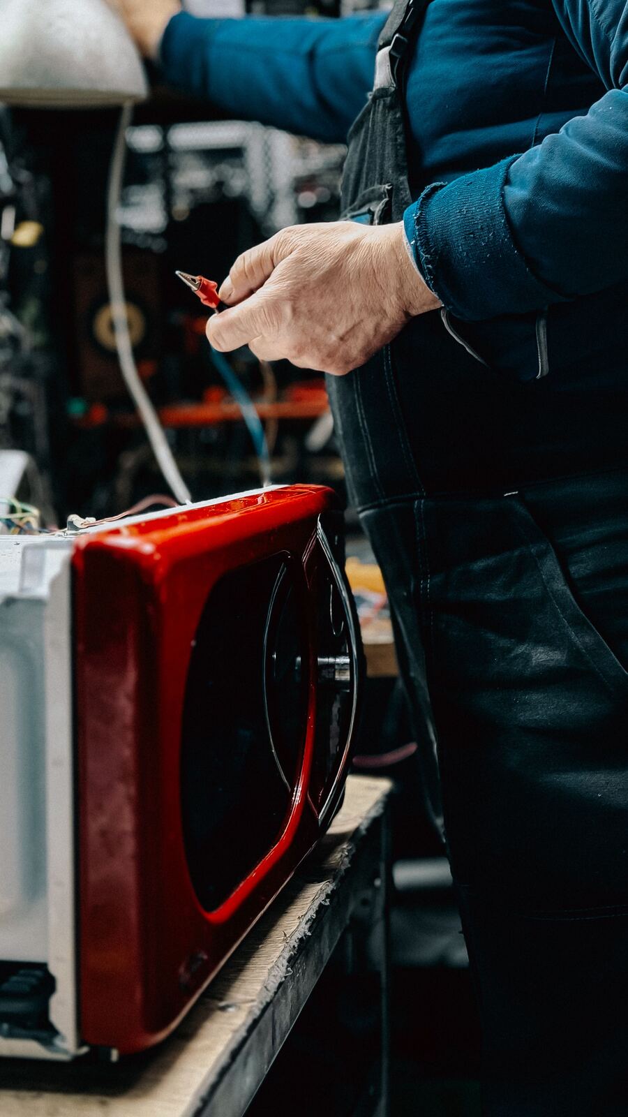 Technician holding a test lead beside a red microwave oven with its outer case removed