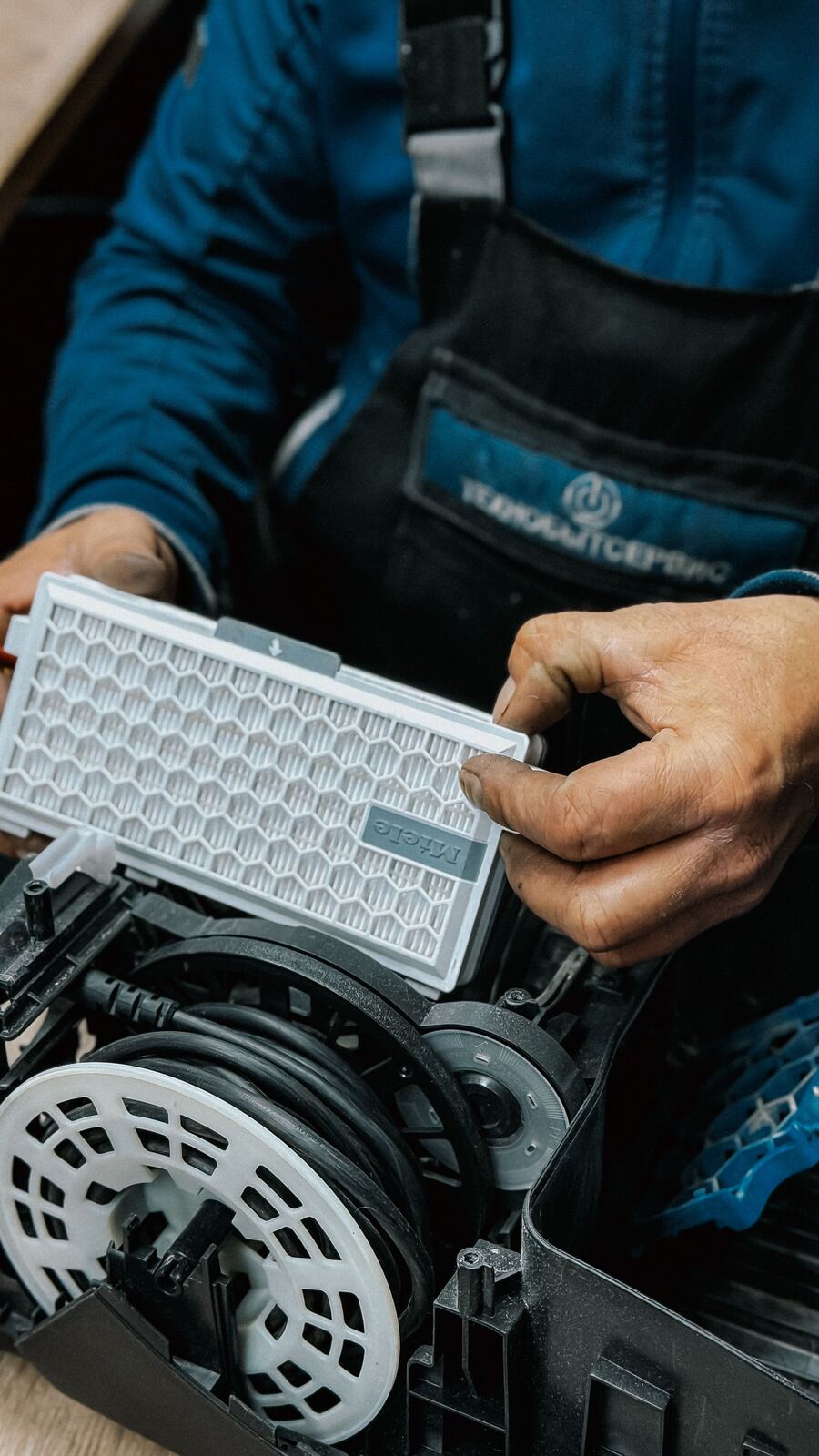 Technician holding a vacuum cleaner filter above the opened body of the machine